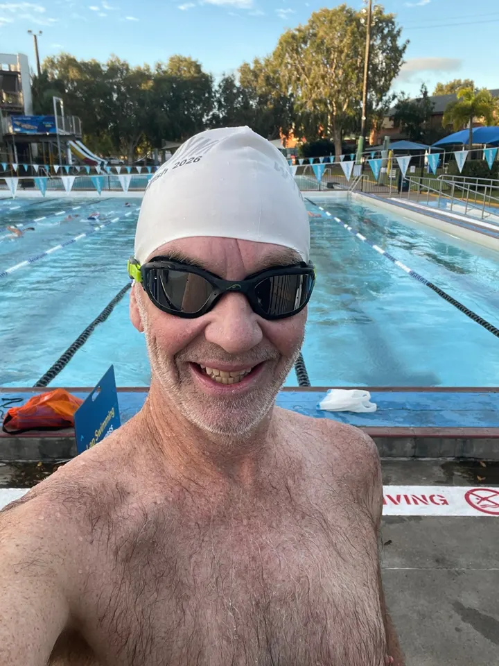 G R., a customer, smiling at an outdoor pool at dawn wearing NanoClear Flex goggles